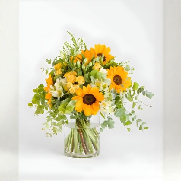 Bouquet of sunflowers and greenery in a clear vase on a white background