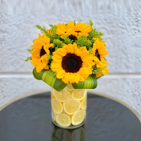 Bouquet of sunflowers in a vase with lemon slices on a reflective surface.