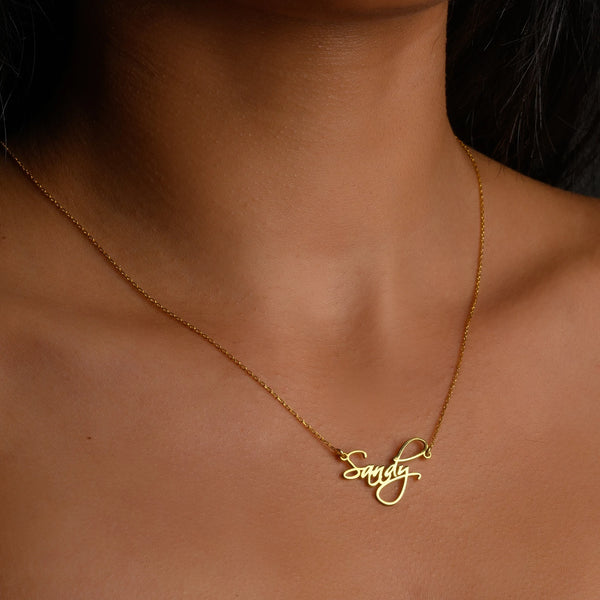 A person wearing a gold-colored necklace with the name 'Sandy' written in a decorative script.