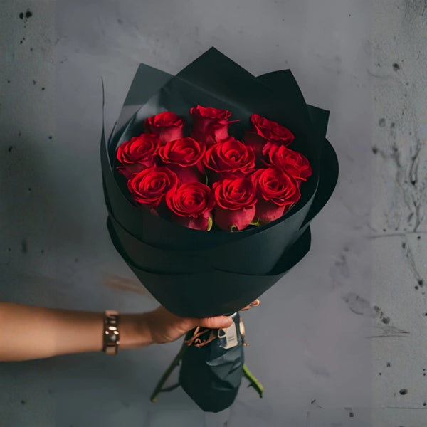 Bouquet of red roses wrapped in black paper held by a person against a gray background